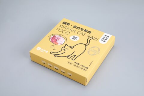 We are a manufacturer of custom box packaging. This image showcases our product: a yellow box designed for Wakaa Cat Raw Food on a sleek gray background. The packaging features an artistic illustration of a cat alongside a bowl filled with raw meat, capturing the essence of the product. The design includes areas designated for nutritional information and product details in multiple languages, ensuring it meets international standards while maintaining functionality and appeal within the packaging industry.