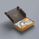 On a grey background, an open Double ClickIt Mailer displays neatly arranged fabric featuring an abstract pattern in orange, black, and white.