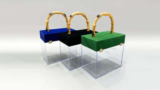 A clear acrylic box featuring a flip-top lid covered in red velvet. It is adorned with a bamboo handle and decorated with a lace bow. The interior contains pink paper filler.