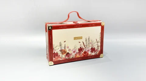 This custom packaging box features a suitcase-style design with a floral motif and red accents, complete with a top handle for easy carrying. Its flip-top style exudes elegance, making it an ideal choice for storing valuables or presenting gifts in a sophisticated manner.
