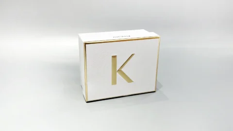 The image showcases a custom box in white and gold with a partially open lid, revealing white raffia inside.