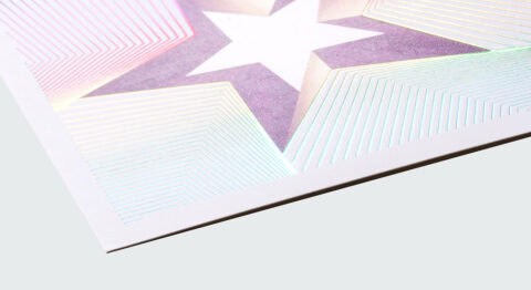 A close-up of a holographic foil stamping on a poster, featuring a star design with a white background and a purple and pink gradient.