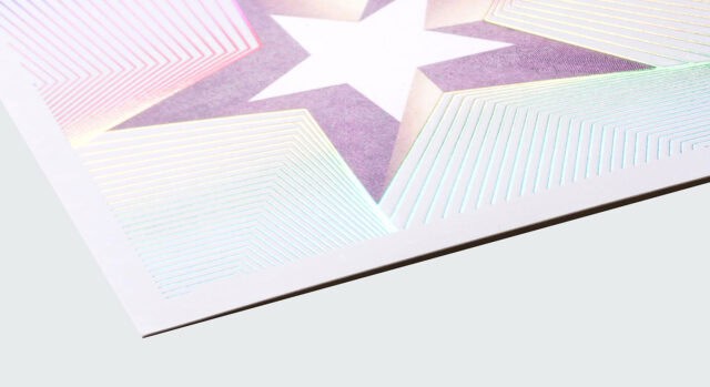 A close-up of a holographic foil stamping on a poster, featuring a star design with a white background and a purple and pink gradient.