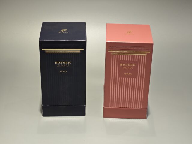 Two rectangular perfume boxes are displayed side by side on a light background. The left box features a dark color scheme with elegant UV printing that highlights its sophisticated design. The right box has a pink hue with gold detailing, both exemplifying exquisite handmade craftsmanship in their construction and finish.