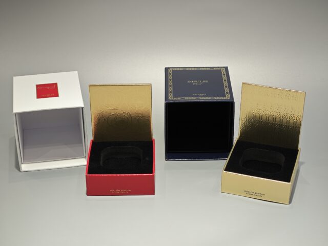 Displayed side by side are two elegant perfume packaging boxes. The box on the left showcases a pristine white finish, while the box on the right features an alluring dark shade. Both boxes are adorned with intricate gold stamping, adding a touch of handmade artistry and luxury to their design.