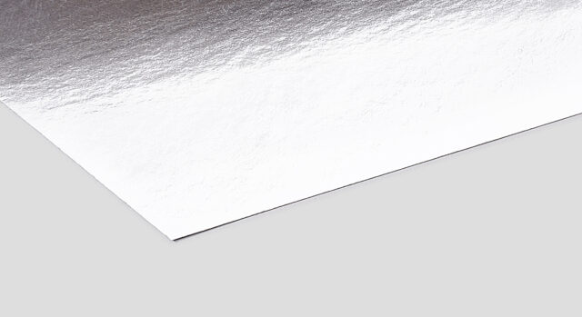 The image portrays a corner section of a sleek, metallic silver packaging material set against a simple gray backdrop.
