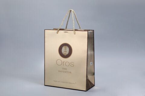 A custom gold packaging box designed with an elegant circular emblem and sturdy rope handles, embodying a sophisticated and inventive aesthetic.