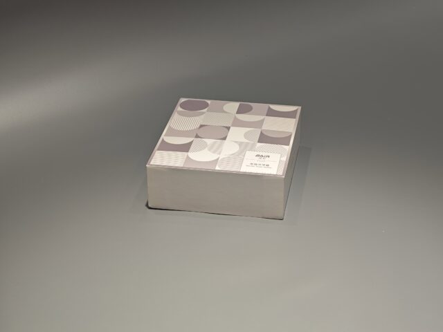 A custom packaging box with a lift-off lid, showcasing an intricate pattern, is displayed elegantly