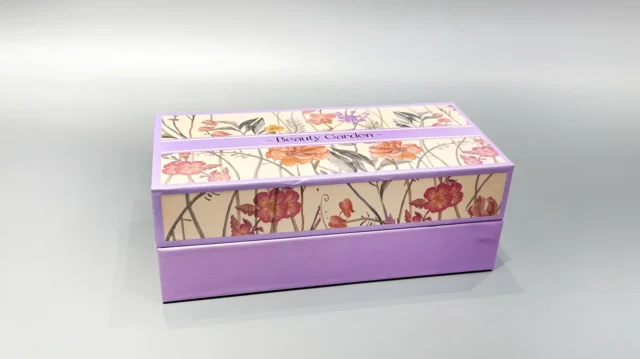 A purple luxury gift box featuring an elegant floral pattern on the lid rests gracefully on a light gray surface.