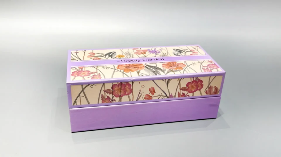 A purple luxury gift box featuring an elegant floral pattern on the lid rests gracefully on a light gray surface.