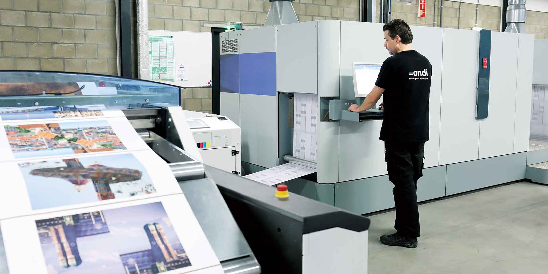 A technician operates a large industrial printer, producing vibrant sheets of custom box packaging in a factory setting.