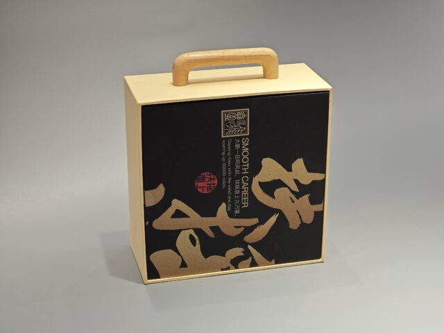 A packaging box with a handle, adorned with black Asian calligraphy and an intricate patterned design.