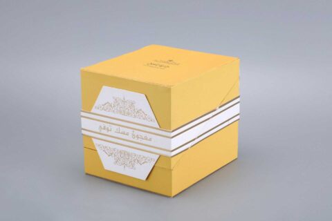 A yellow packaging box with decorative white and gold accents, featuring distinctive design elements on the front.