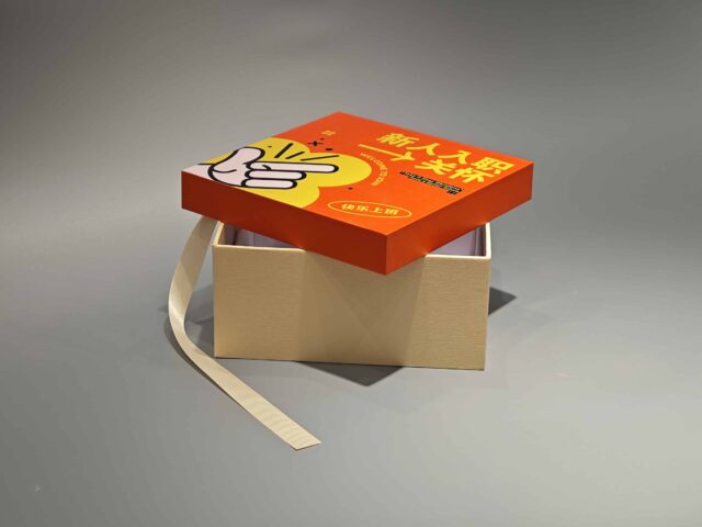 Beige custom packaging box with a detachable orange lid, featuring an artistic design and adjacent loose ribbon