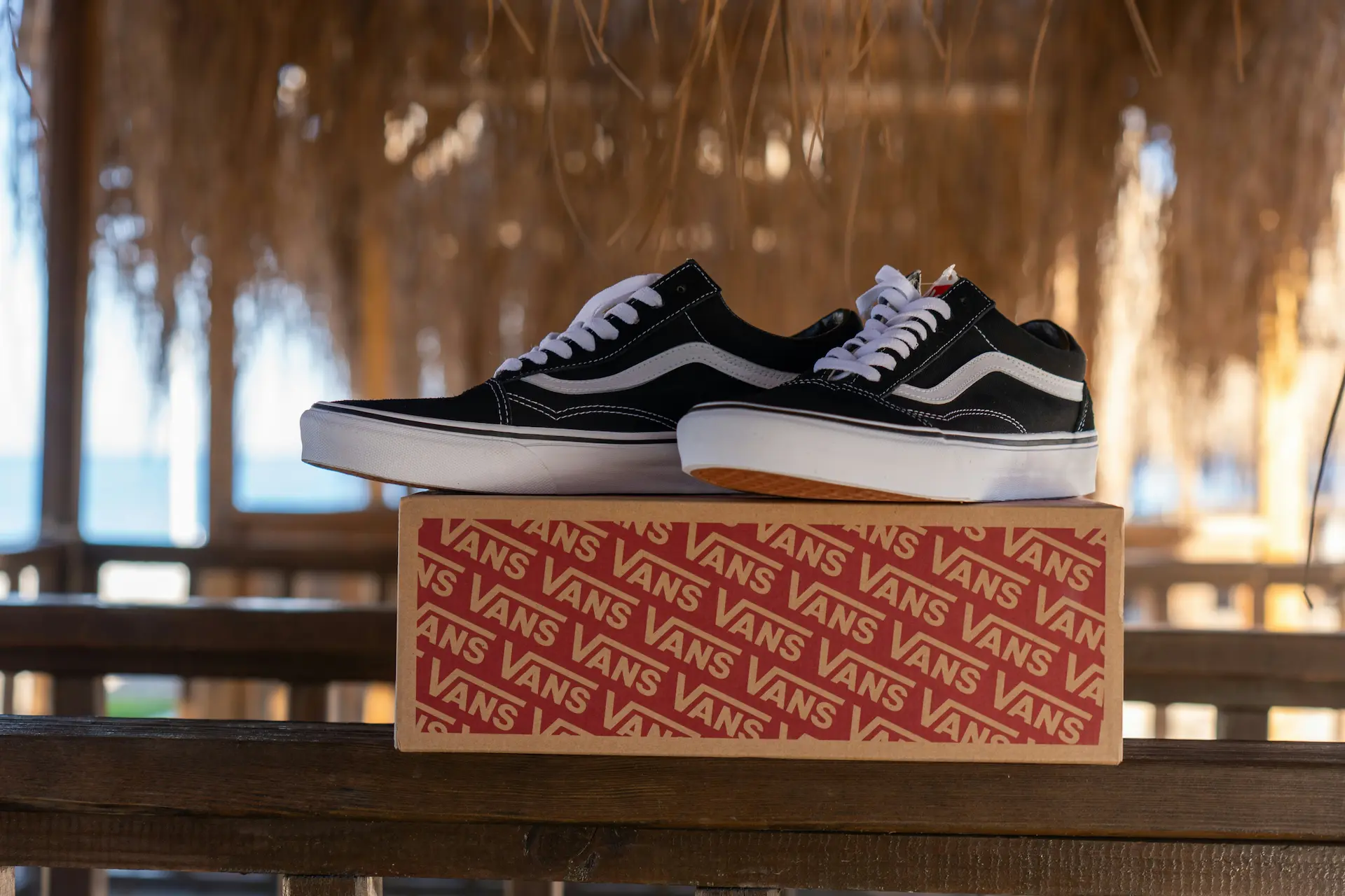 Black and white Vans sneakers on a box, ready to ship under a thatched roof.