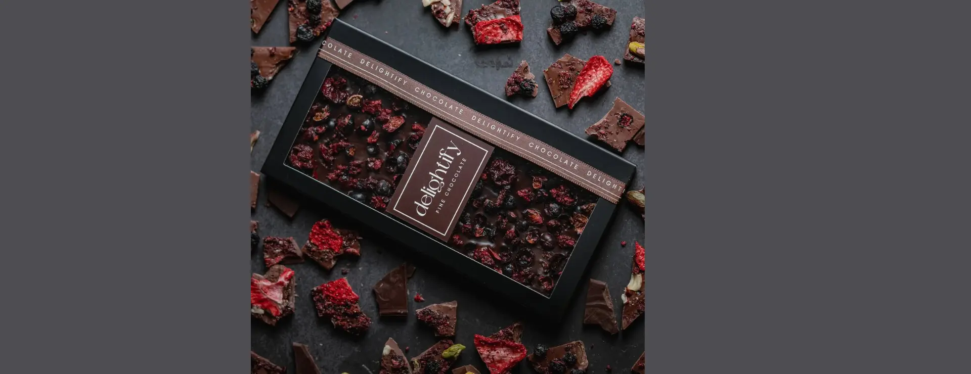 Box of dark chocolate with berries in elegant chocolate packaging and dried strawberries.