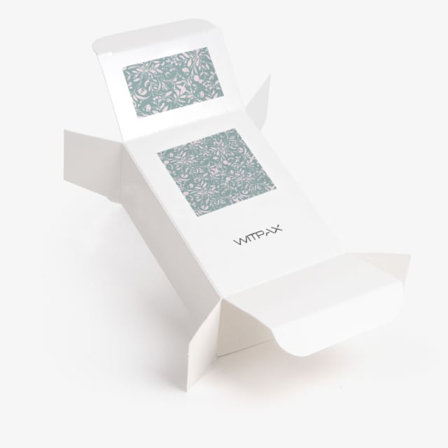 Custom white folding carton with decorative teal pattern windows shown in open position displaying interior compartments