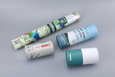 Four custom-designed cylindrical packaging boxes in various colors are showcased against a gray background.