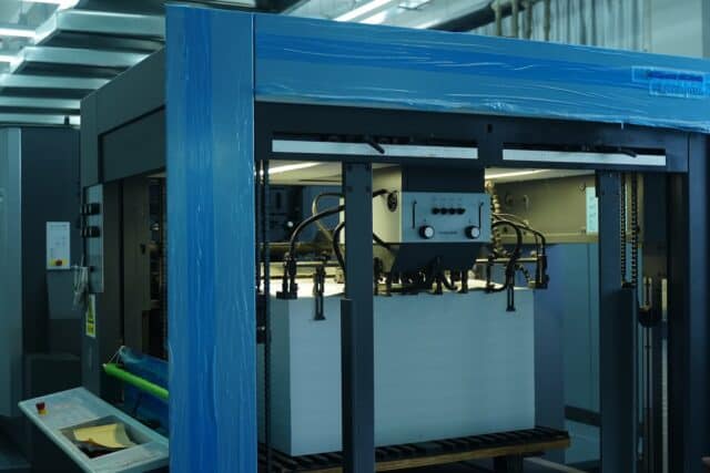 Large industrial printer with stacked sheets under bright lighting.