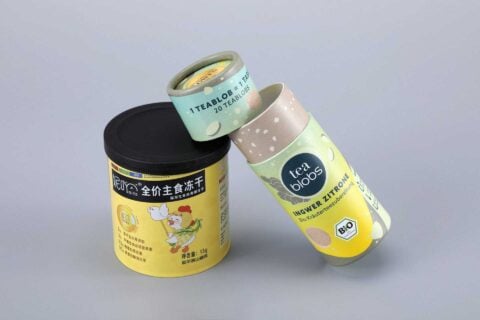 Our custom box packaging includes three cylindrical tea containers. One is designed in a vibrant yellow featuring an illustrated chef, while the other two come in soft pastel shades with unique brand motifs and detailed descriptions.