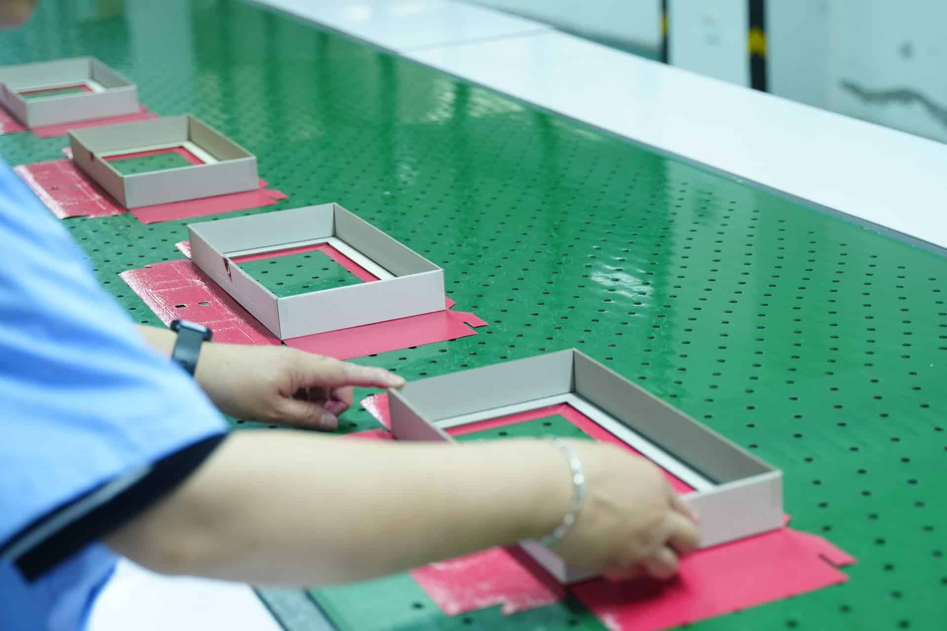 Person assembling boxes on a green perforated surface.