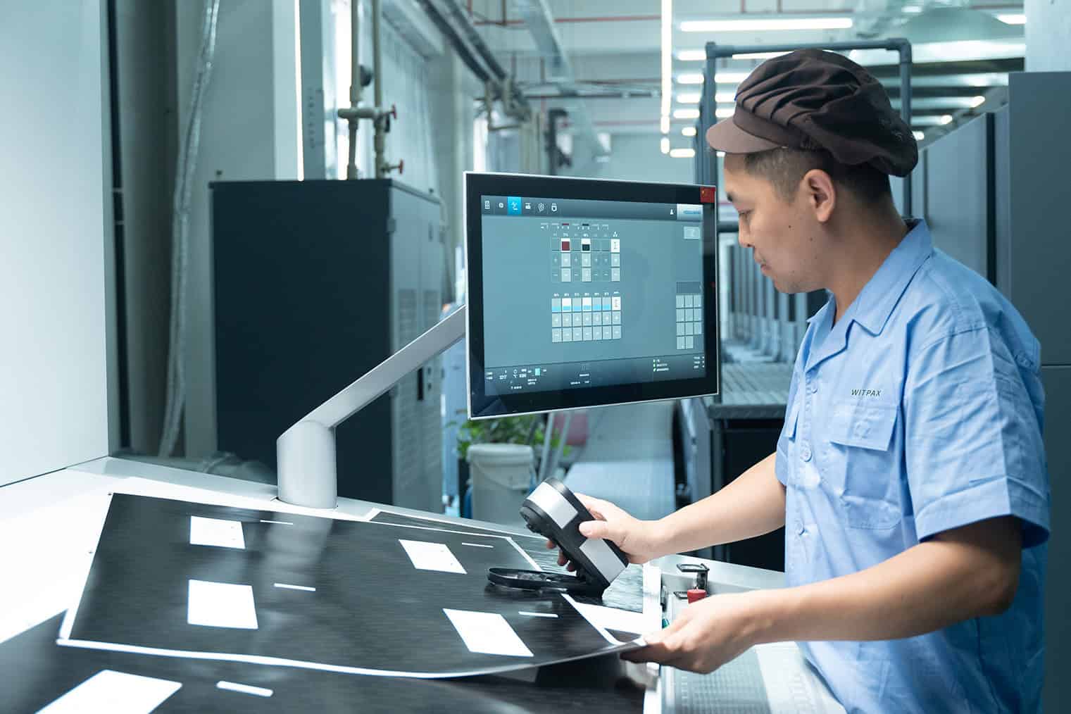 Person inspecting printed materials at a workstation with a computer monitor.