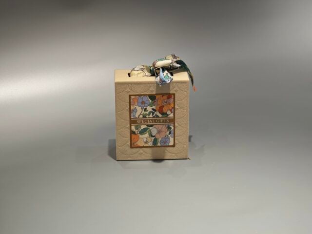a beige custom box with a floral pattern. It features a decorative ribbon elegantly tied at the top, enhancing its presentation as a gift packaging solution.