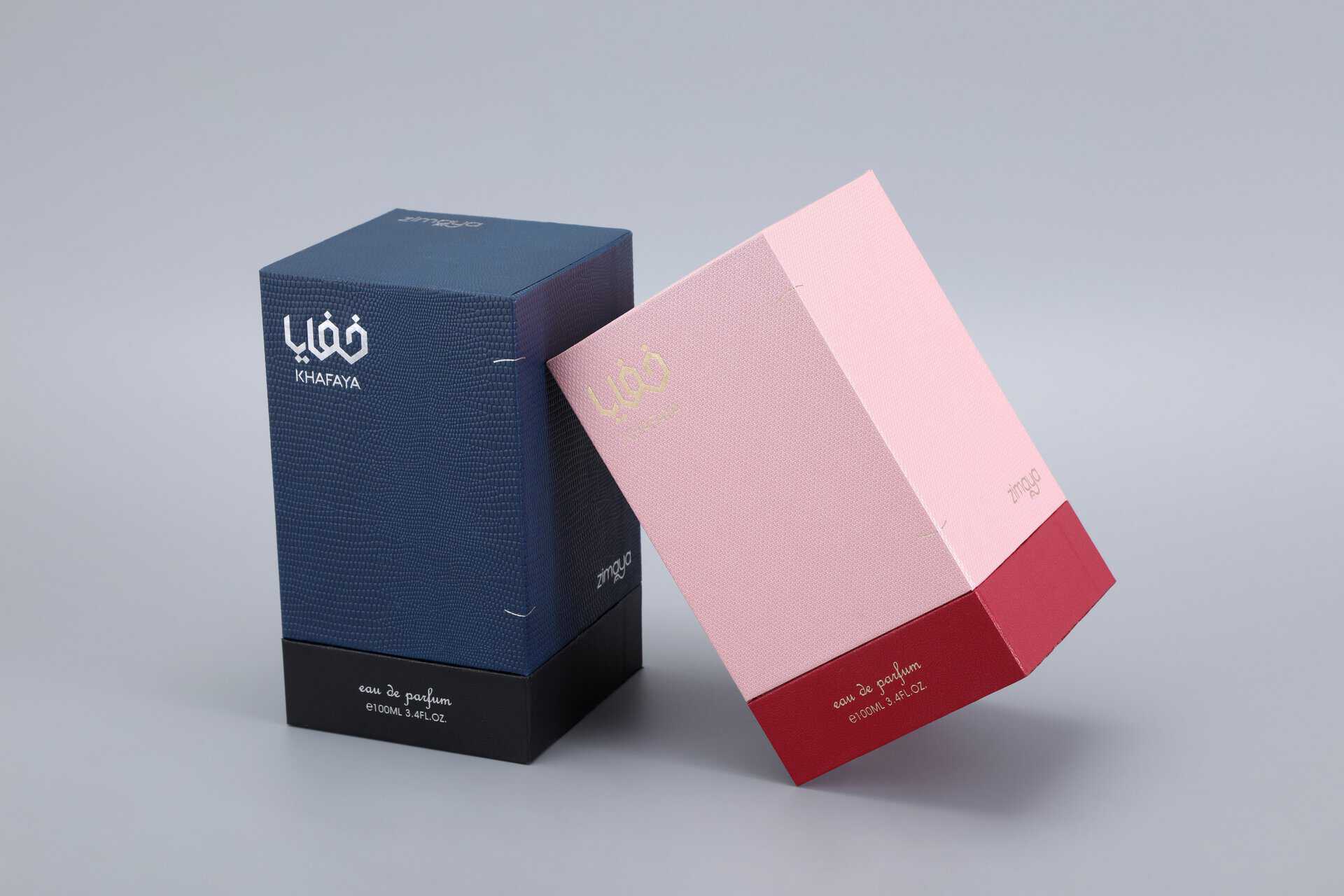 The image depicts two custom-designed, upright perfume boxes in navy and pink colors, showcasing elegant Arabic motifs against a gray background.