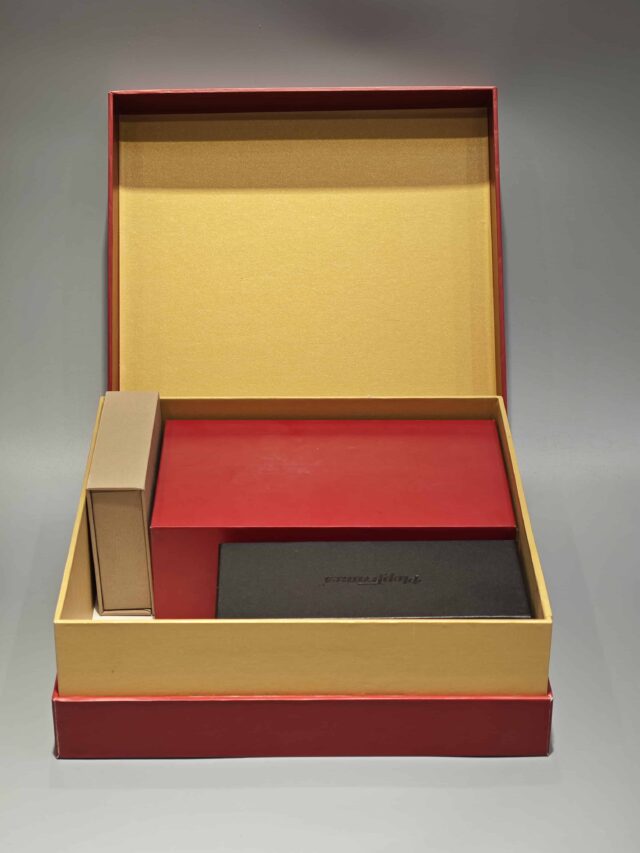 The image showcases a vibrant red and yellow custom packaging solution, featuring an open gift box that reveals a bespoke red rigid box and an included flat package.