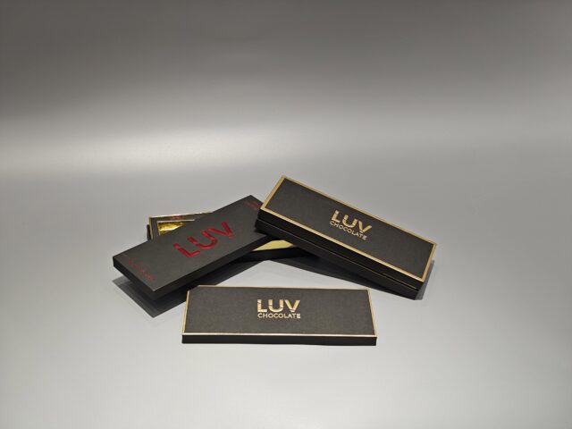 A rectangular black custom box designed for chocolate products is showcased on a smooth, gray surface.