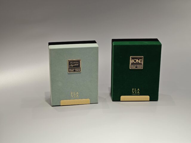 The image showcases two exquisite custom packaging boxes for Flavia perfume. One box features a light green design with silver accents, while the other is dark green with gold accents, both incorporating elegant foil stamping details.