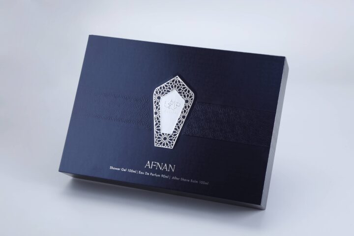 The product is a navy blue box with an elaborate white geometric pattern, showcasing the brand identity "Afnan." It contains shower gel, eau de parfum, and after shave balm.