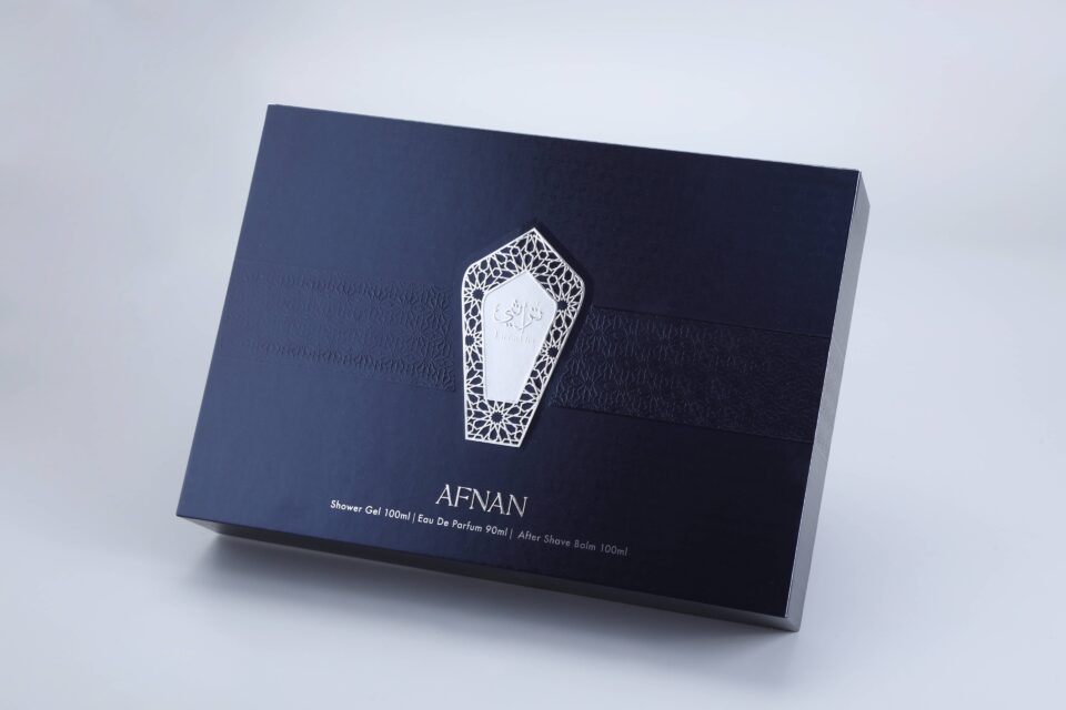 The product is a navy blue box with an elaborate white geometric pattern, showcasing the brand identity "Afnan." It contains shower gel, eau de parfum, and after shave balm.