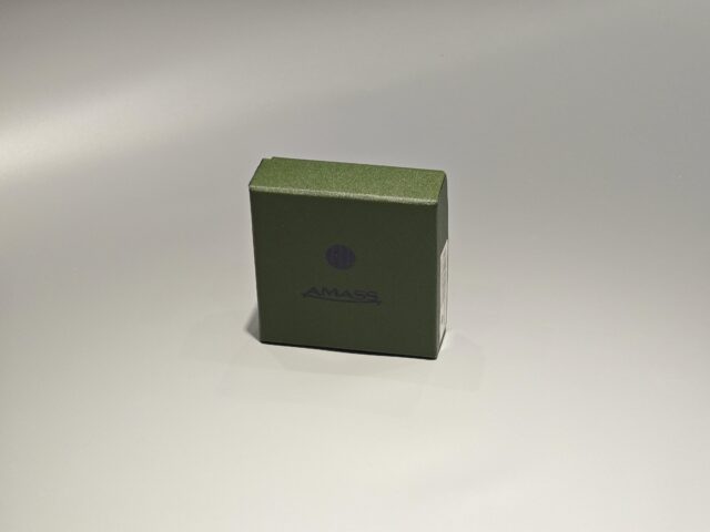 The product is a small green custom box designed with a lift-off lid, suitable for packaging needs. The box features minimalist branding on the front and is set against a plain background.