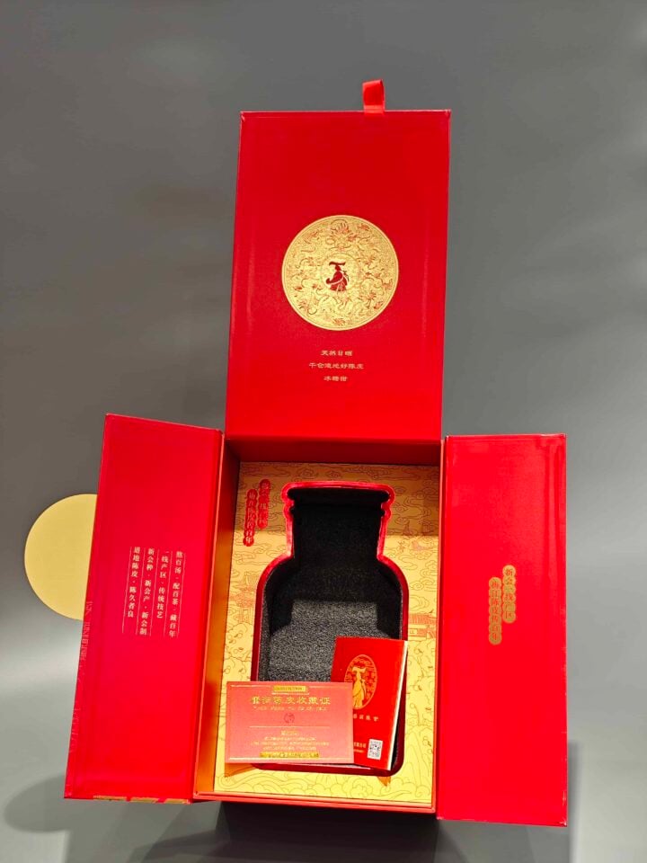 This image displays our custom packaging product: a red and gold decorative box with a hinged lid. Inside, the design highlights an area for bottle placement and includes an insert for additional components.