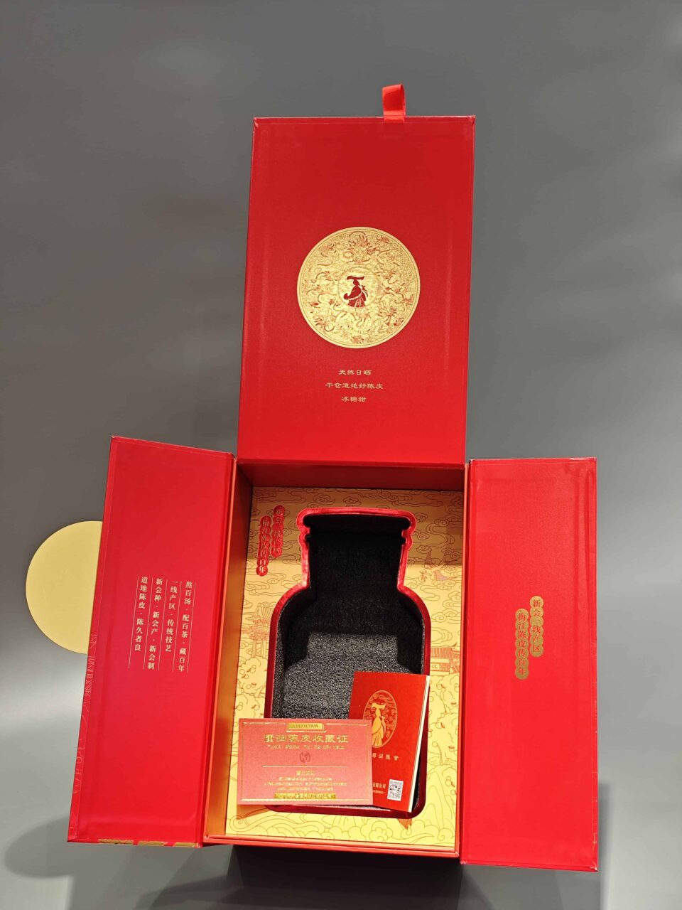 This image displays our custom packaging product: a red and gold decorative box with a hinged lid. Inside, the design highlights an area for bottle placement and includes an insert for additional components.