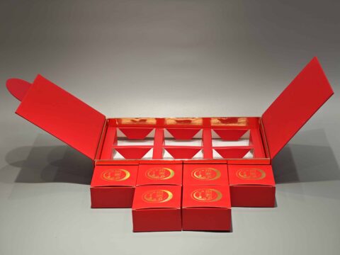 This image represents our custom packaging product: A red compartmentalized box featuring six double-sided sections, each containing a smaller red box adorned with a circular gold emblem design.
