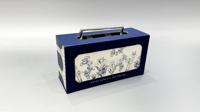 This is a custom-designed blue packaging box featuring a floral pattern and a metal handle. Its charming design gives it the appearance of a portable gift box, making it an attractive option for various occasions.