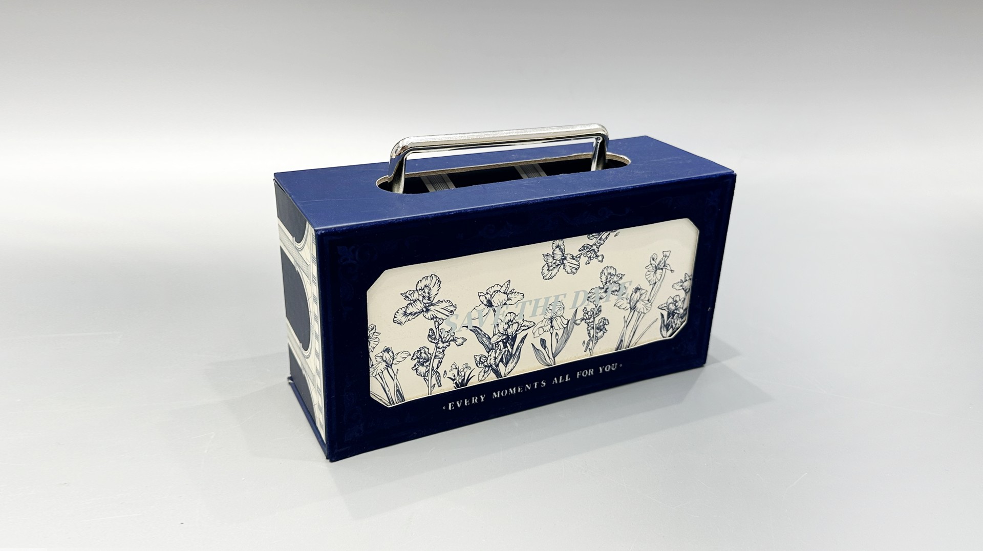 This is a custom-designed blue packaging box featuring a floral pattern and a metal handle. Its charming design gives it the appearance of a portable gift box, making it an attractive option for various occasions.