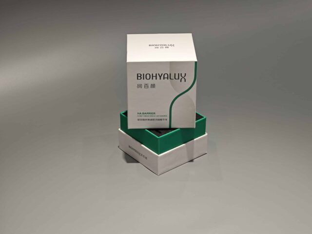 Two custom skincare packaging boxes are stacked on a gray surface, with their lift-off lids slightly ajar. The boxes showcase intricate designs and craftsmanship.