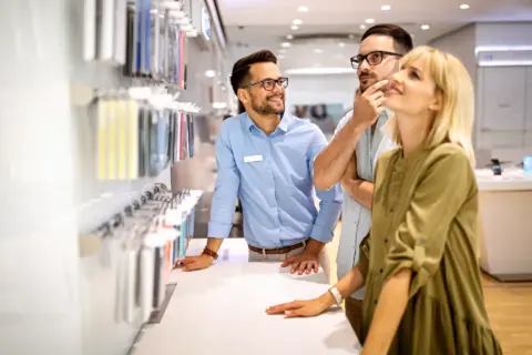 Two customers look at phone accessories while a store employee assists them.