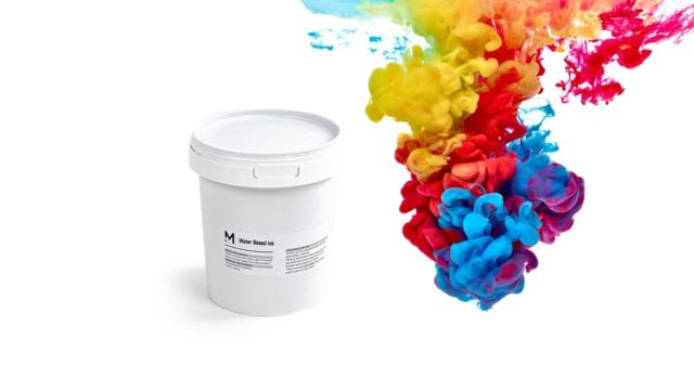 Water-based inks bloom vibrantly beside a white paint bucket in water.