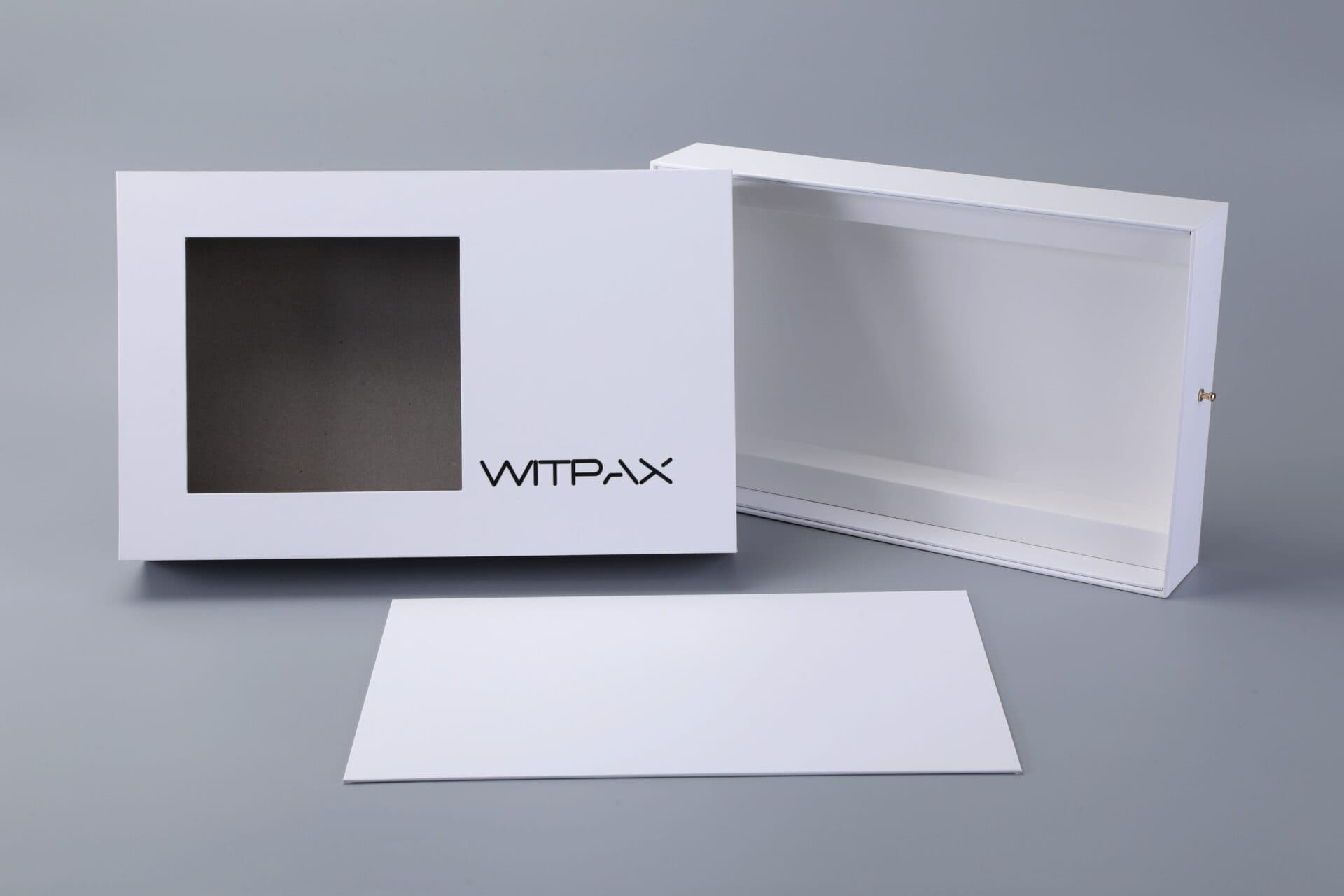 White drawer box with window, open lid, and separate flat piece on a gray surface.