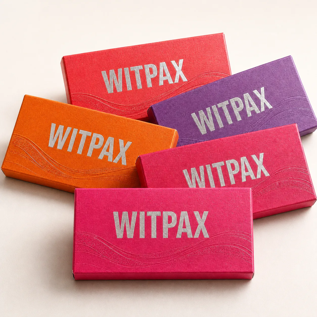 Five colorful WITPAX cosmetic folding cartons with silver foil logos and embossed wave textures under bright studio lighting.
