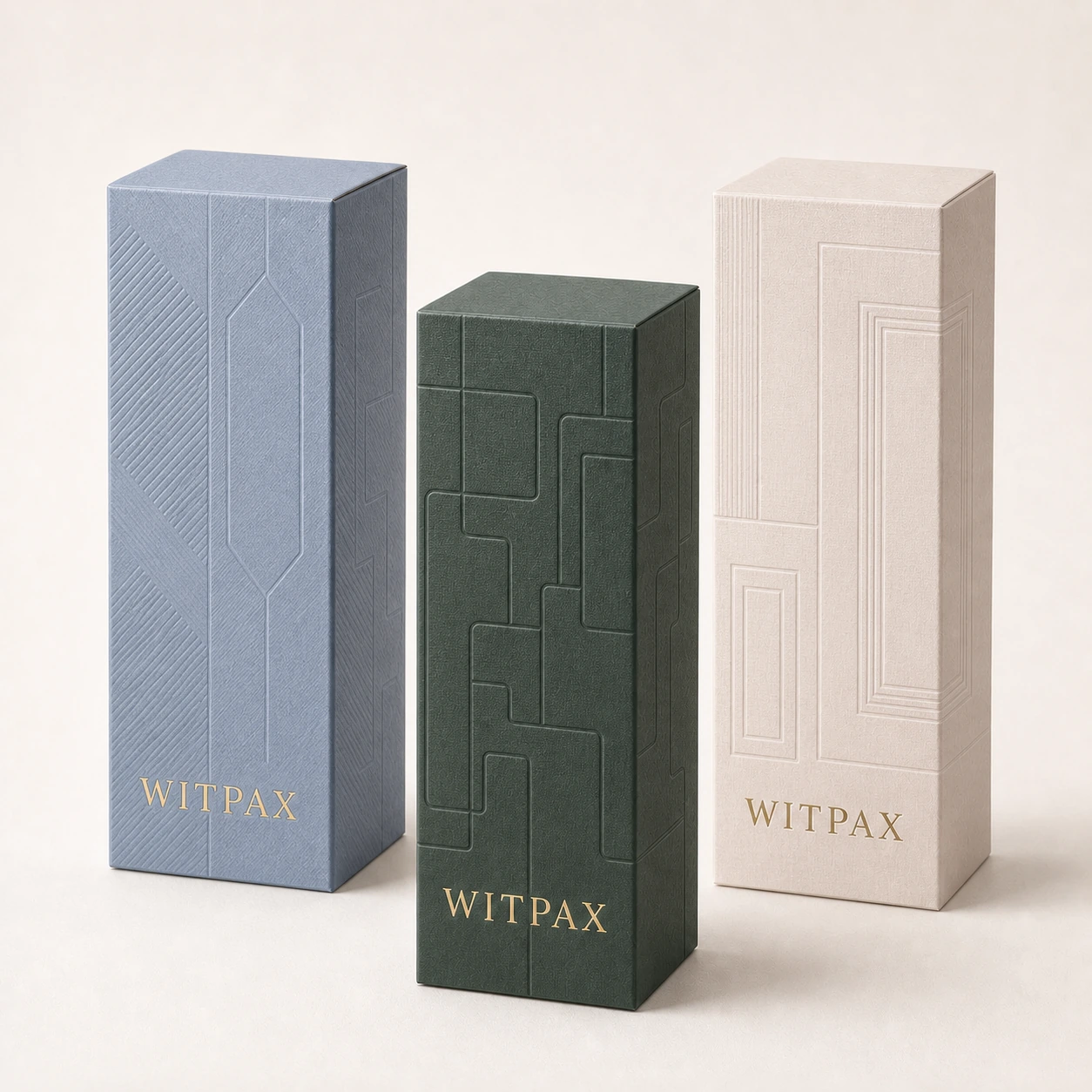 Three tall WITPAX cosmetic cartons in blue, forest green, and ivory with gold foil logos and geometric embossed patterns.