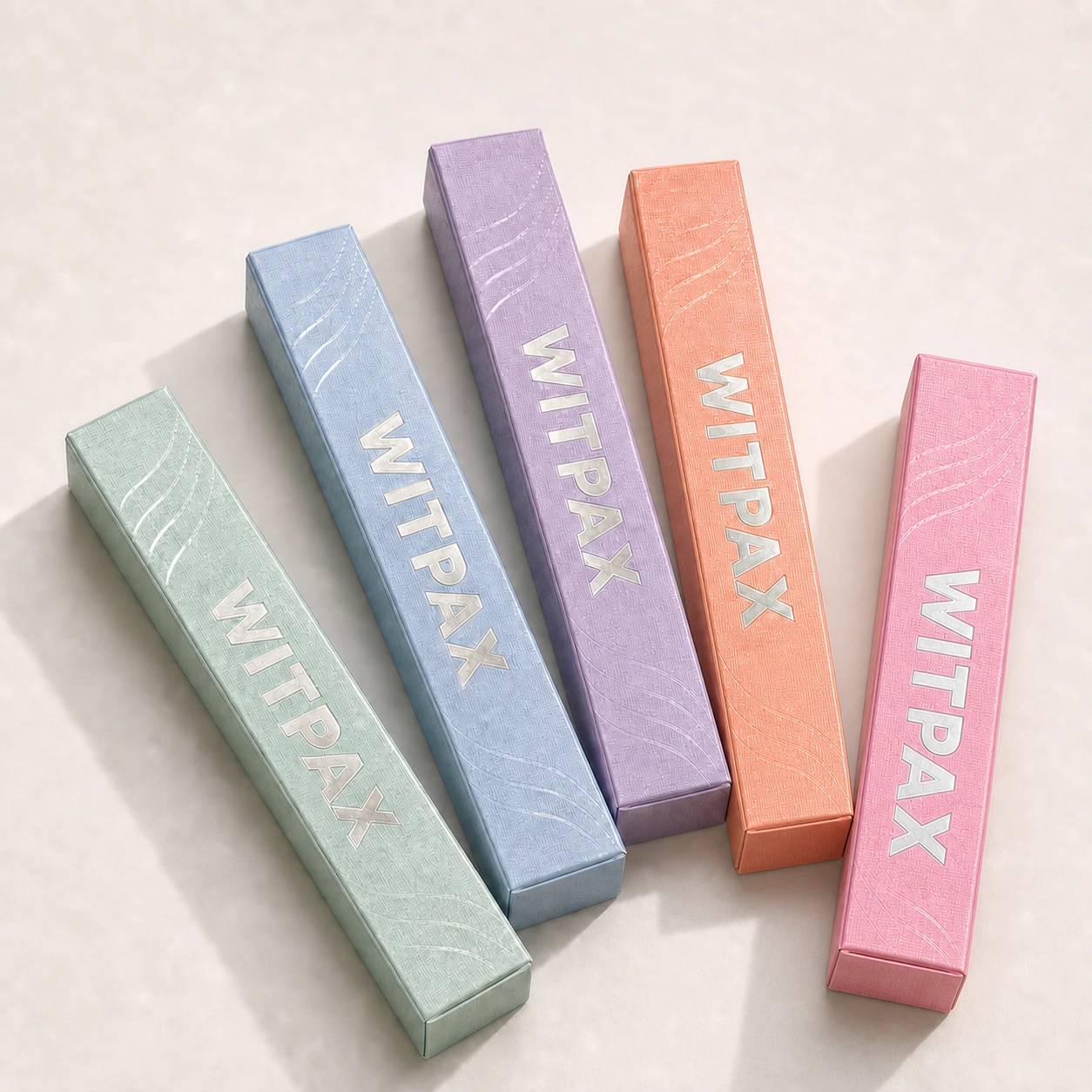 Five separated pastel WITPAX cosmetic cartons with silver foil logos and embossed wave textures under bright studio lighting.