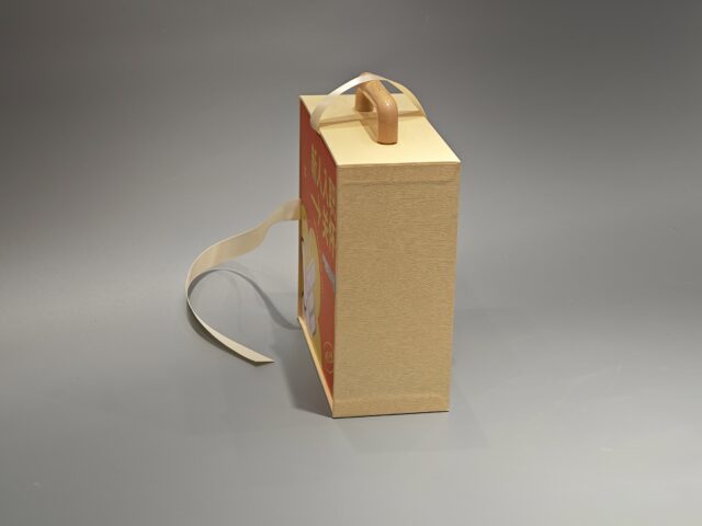 Beige custom packaging box with a detachable orange lid, featuring an artistic design and adjacent loose ribbon