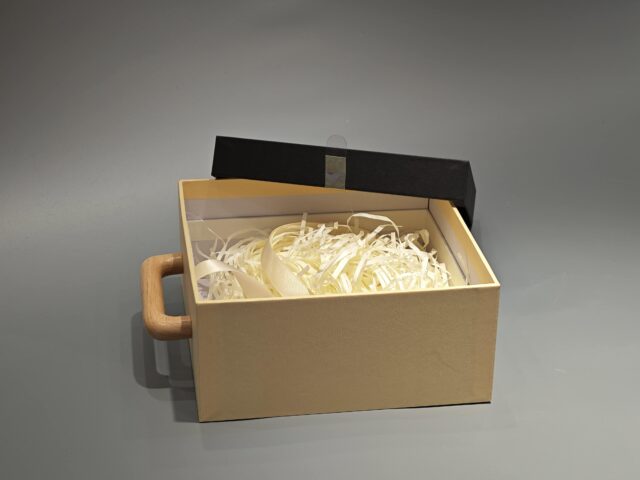 A packaging box with a handle, adorned with black Asian calligraphy and an intricate patterned design.