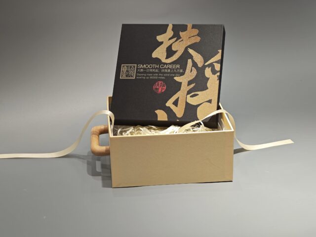 A packaging box with a handle, adorned with black Asian calligraphy and an intricate patterned design.
