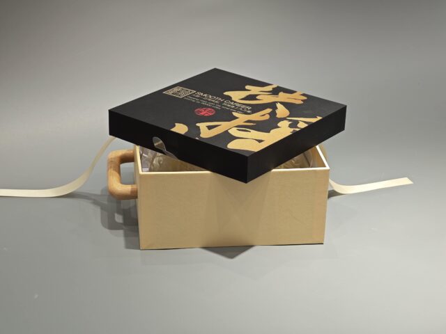 A packaging box with a handle, adorned with black Asian calligraphy and an intricate patterned design.